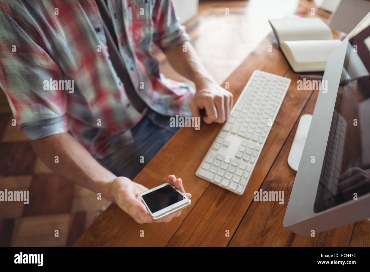 L'homme assis à un bureau et ordinateur looking at mobile phone Banque D'Images