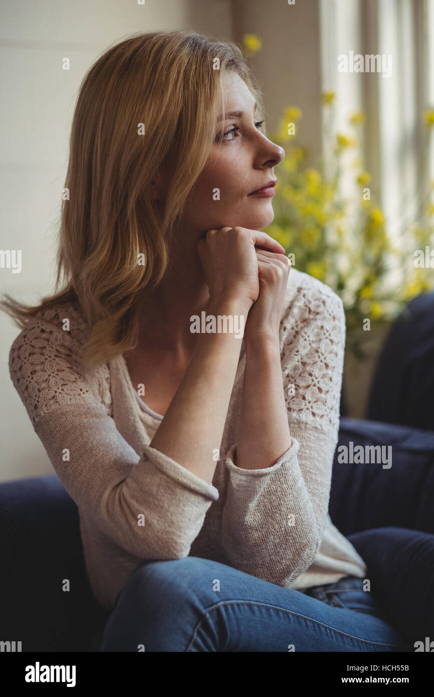 Thoughtful woman sitting on sofa in living room Banque D'Images