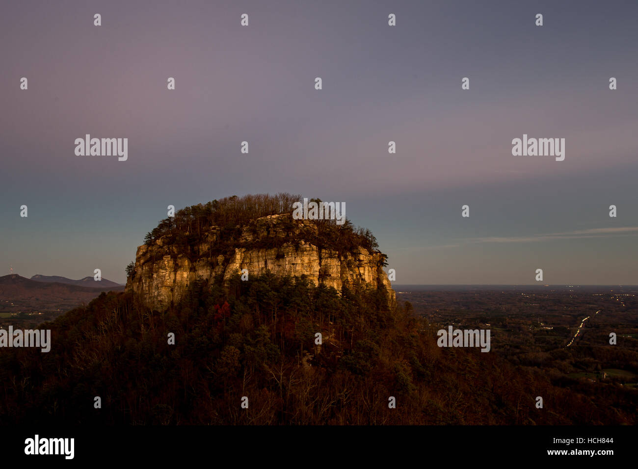 Gros pinacle de Pilot Mountain en Caroline du Nord, USA avec coucher du soleil nuages roses et des lumières de voitures sur une autoroute dans la distance Banque D'Images