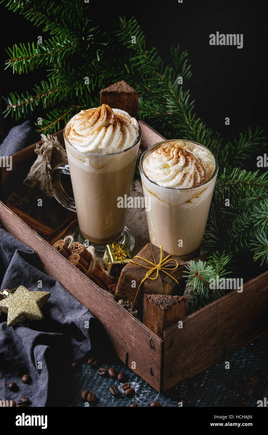 Latte épicé à la citrouille avec crème fouettée et de cannelle dans deux verres debout dans planche de bois avec du textile et de décoration de Noël et de sapin autres Banque D'Images