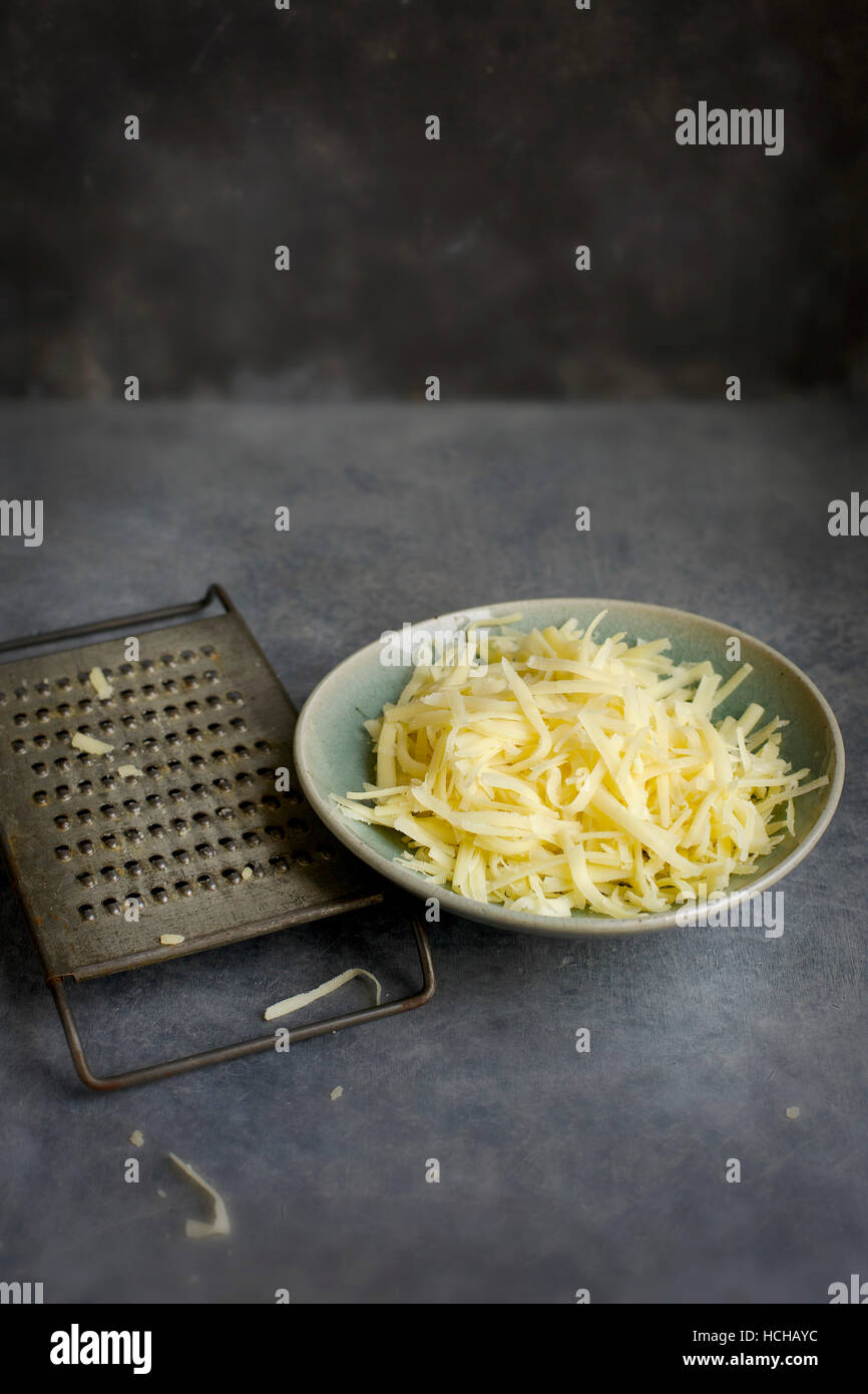 Bol en céramique de fromage râpé avec Vintage râpe à fromage, photographiée sur fond gris en vue de dessus. Banque D'Images