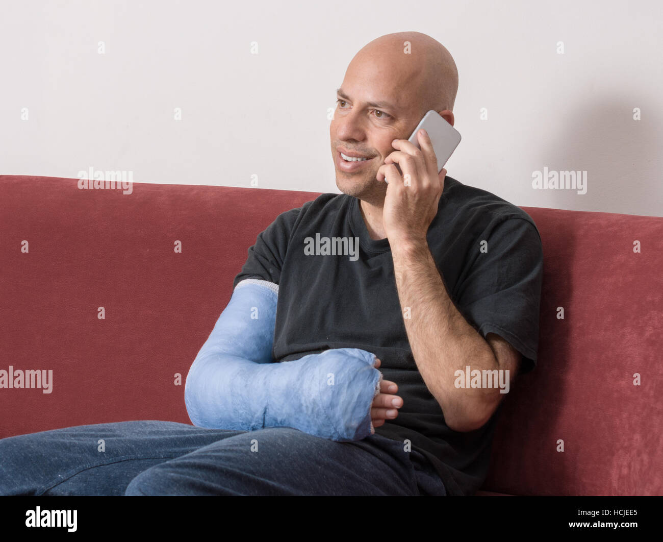 Jeune homme avec un bras et coude dans un plâtre bleu / plâtre en fibre de verre à la maison, heureux de parler sur son téléphone après avoir cassé le bras Banque D'Images