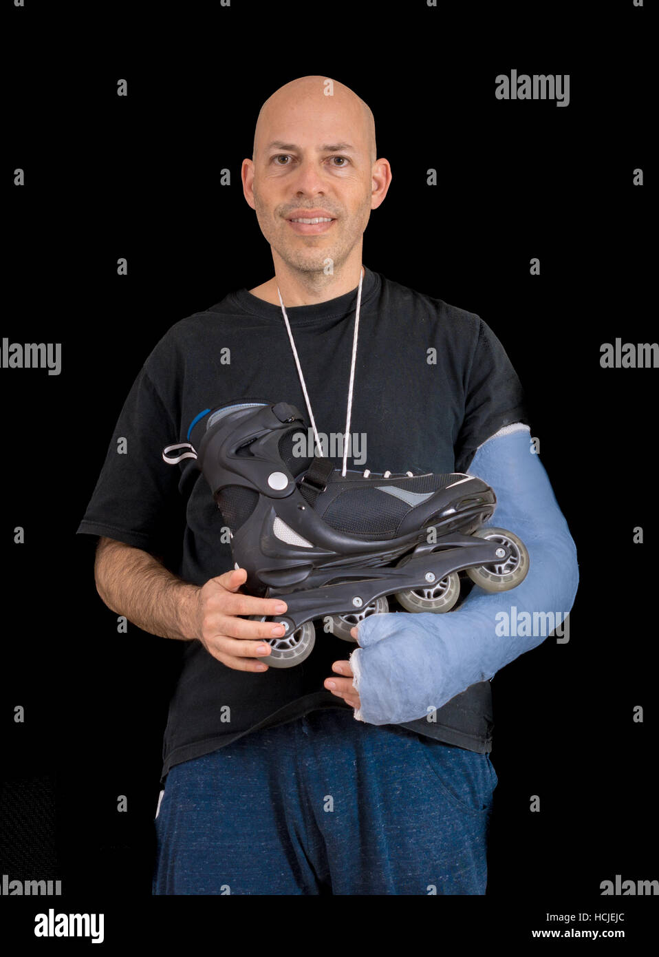 Jeune homme portant un bras bleu vif exprimés, la tenue d'une inline skate une effraction son bras dans un accident de patin à roues alignées, isolé sur fond noir Banque D'Images