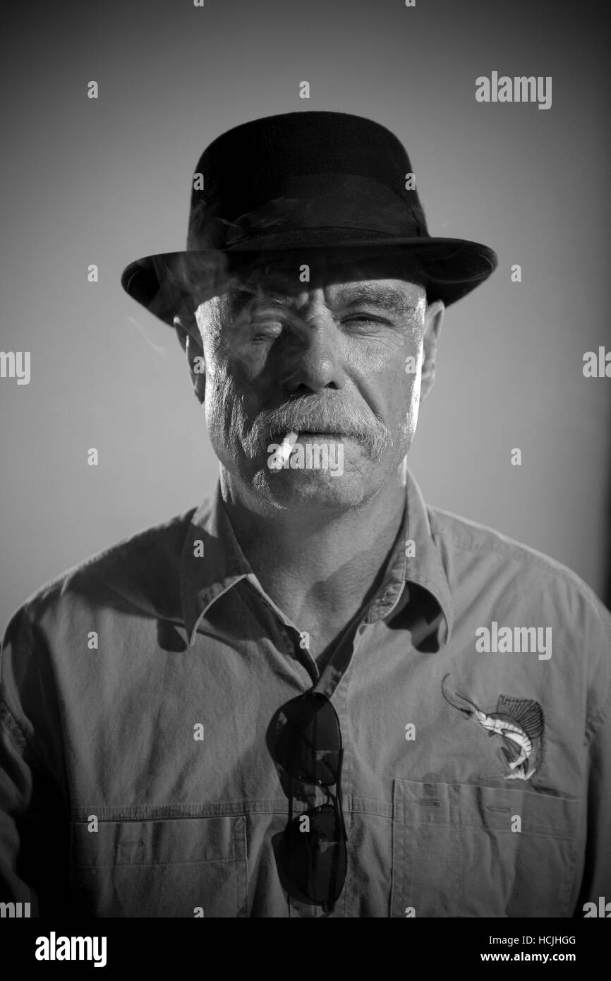 Un vétéran homme portant un chapeau fouines en fumant une cigarette. Banque D'Images