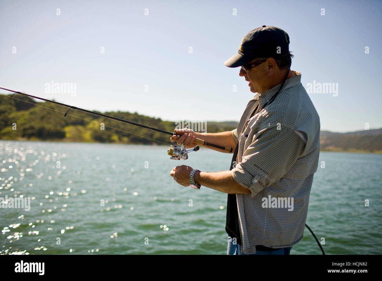 Un homme se tient sur un bateau avec canne à pêche dans la main tandis que la pêche basse dans le lac Casitas Banque D'Images