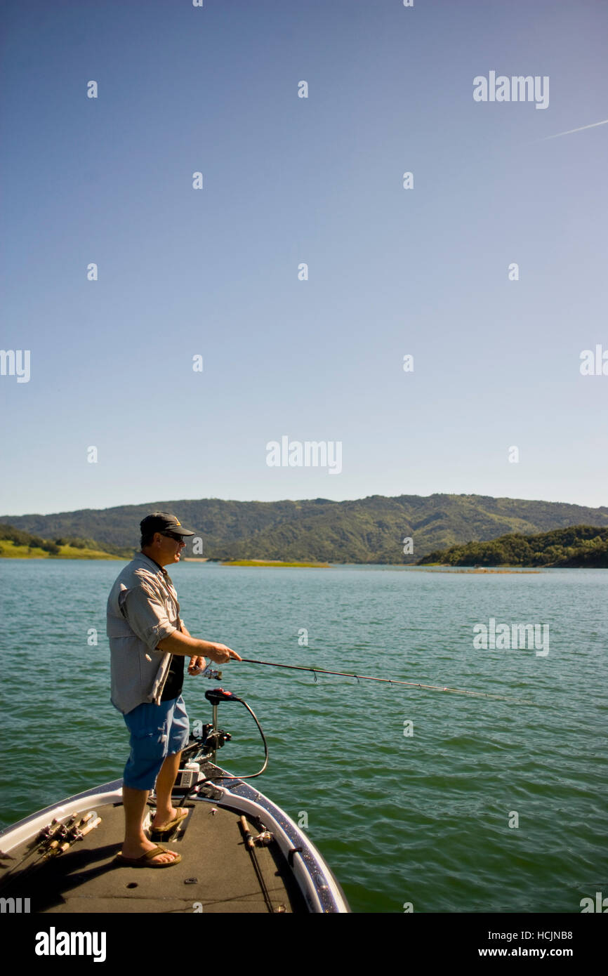 Un homme se tient sur un bateau avec canne à pêche dans la main tandis que la pêche basse dans le lac Casitas Banque D'Images