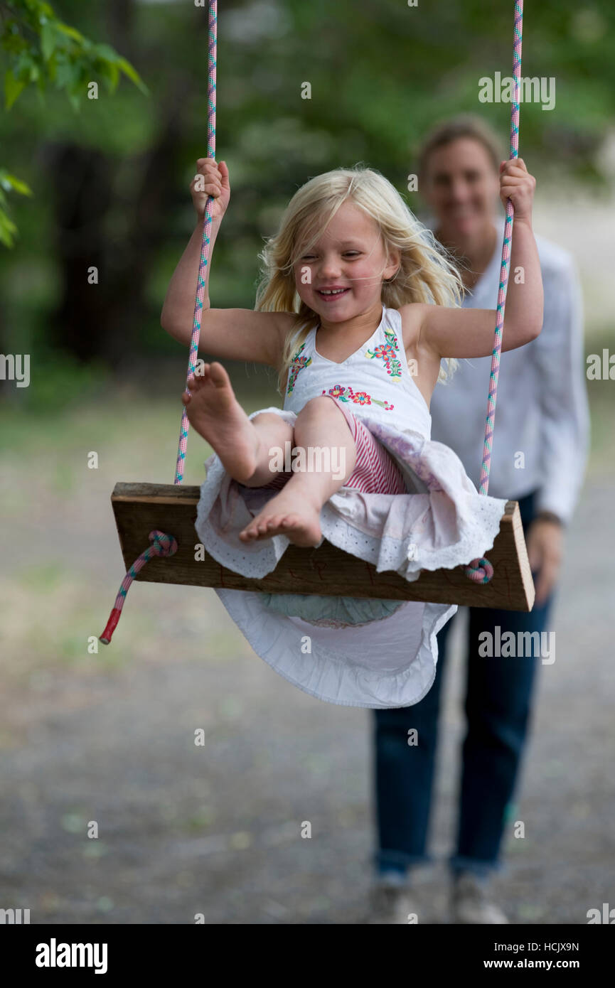 Blonde, pieds nus petite fille portant une robe d'été est poussée par sa  mère sur une balançoire sur une journée d'été Photo Stock - Alamy