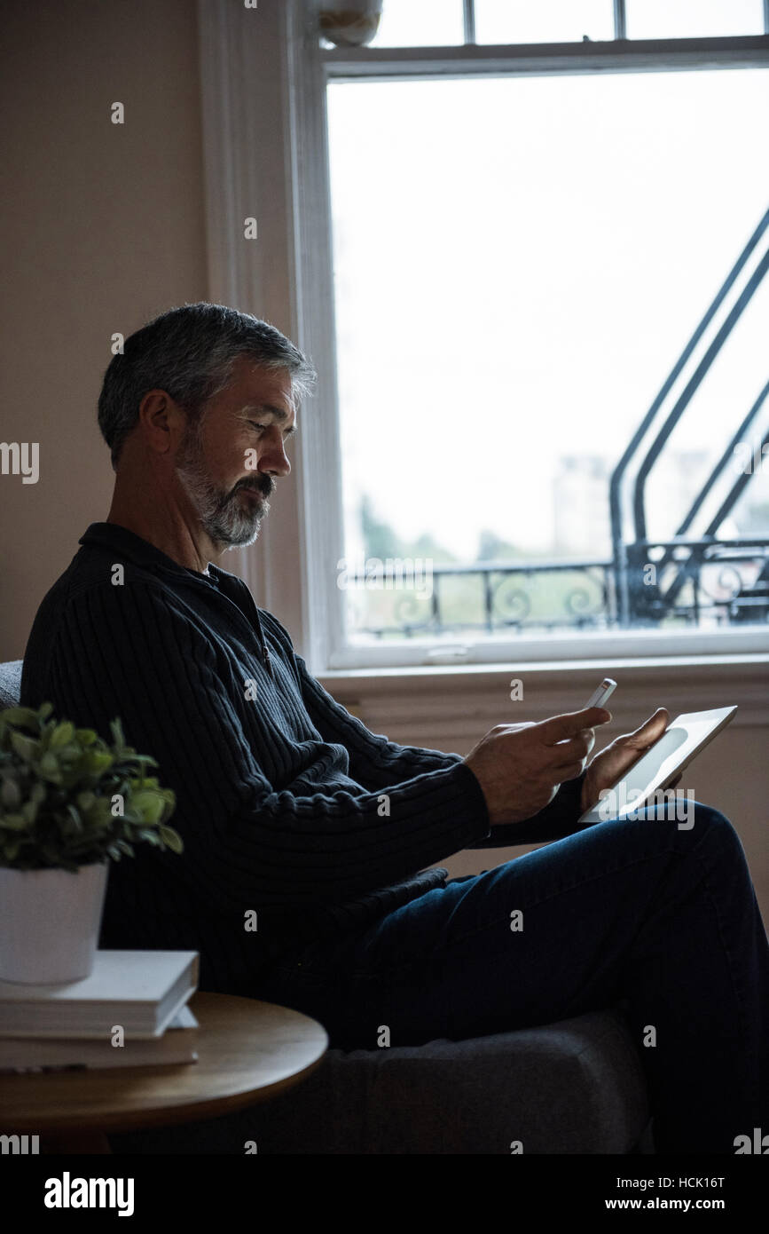 L'homme en utilisant mobilephone et digital tablet in living room Banque D'Images