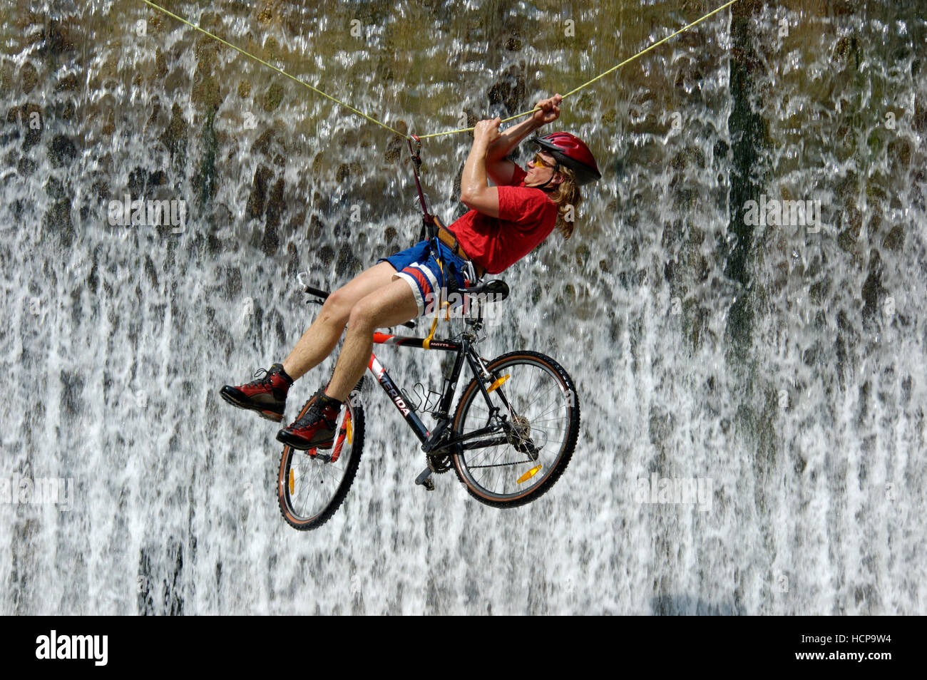 Man crossing une cascade sur une corde avec un vélo Banque D'Images