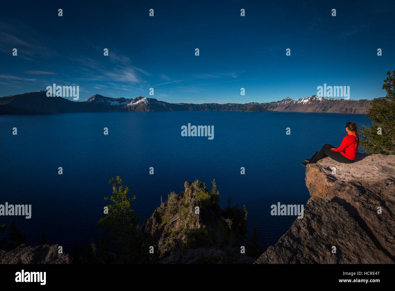 Femme assise sur le bord d'une falaise à la recherche dans le lac du cratère Oregon Banque D'Images
