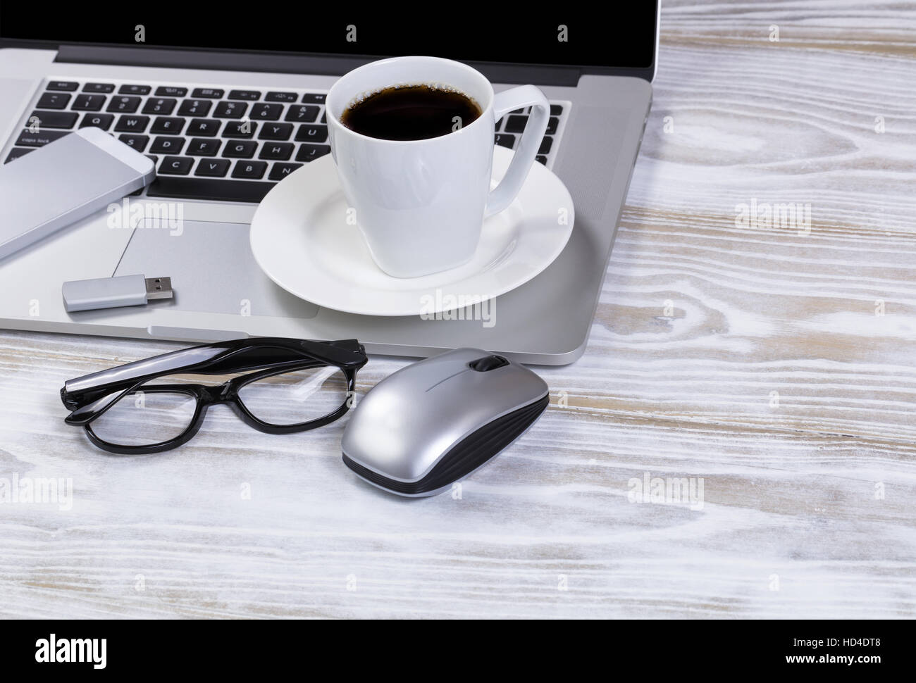 Close up de café du matin sur le dessus de bureau avec ordinateur portable Clavier, clé usb, lunettes de lecture, et de téléphone cellulaire. Banque D'Images