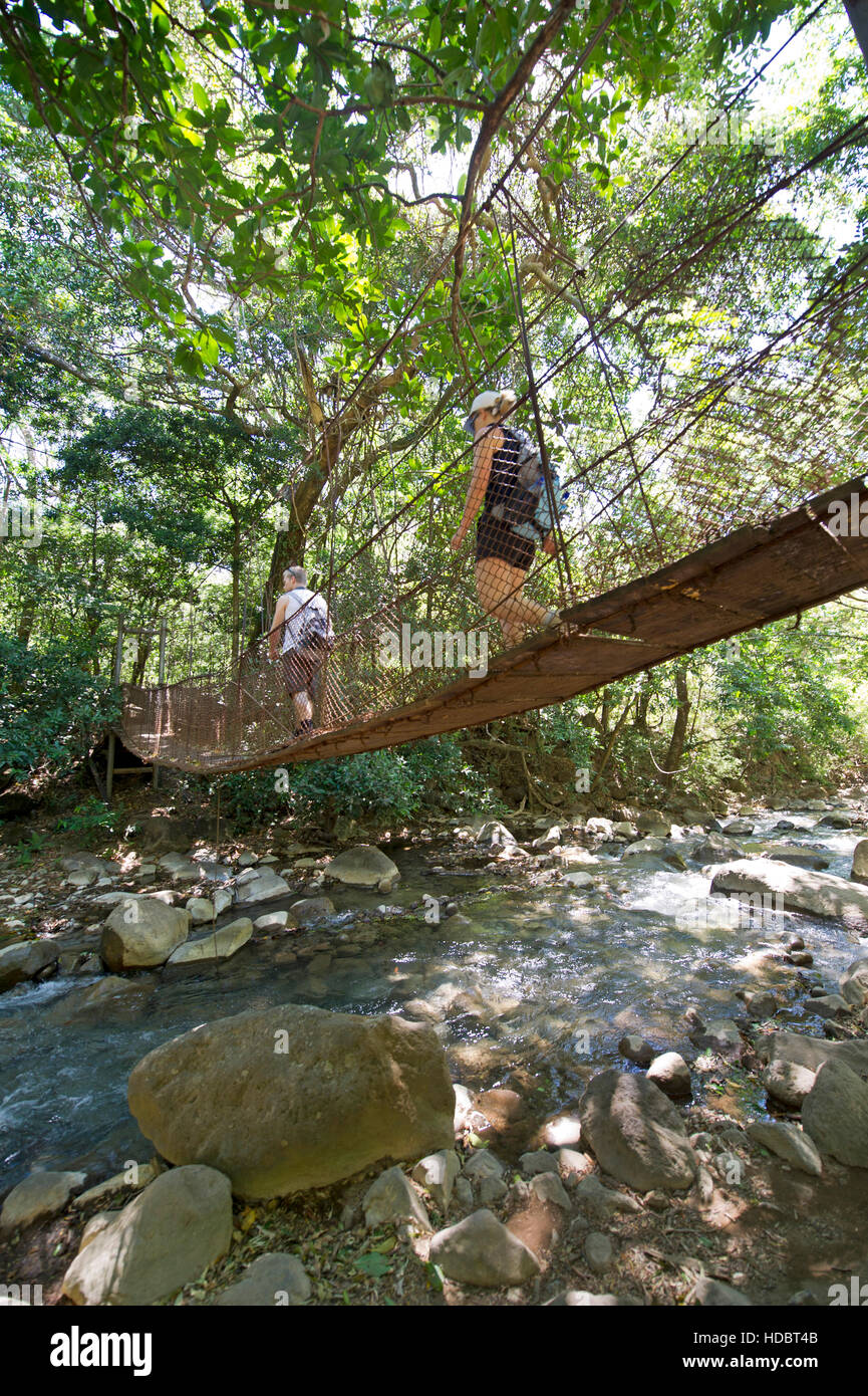 Les touristes marcher sur un pont suspendu à travers Rio Colorado dans Rincon de la Vieja Volcano National Park au Costa Rica. Banque D'Images