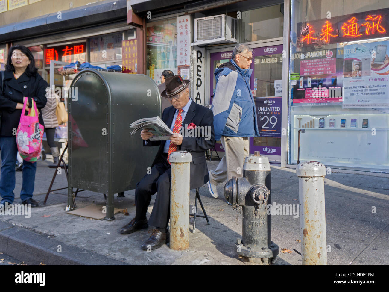 Un homme d'âge moyen habillé bien lire un journal ethnique sur Roosevelt Avenue dans le quartier chinois, le centre-ville, le rinçage, Queens, NYC Banque D'Images