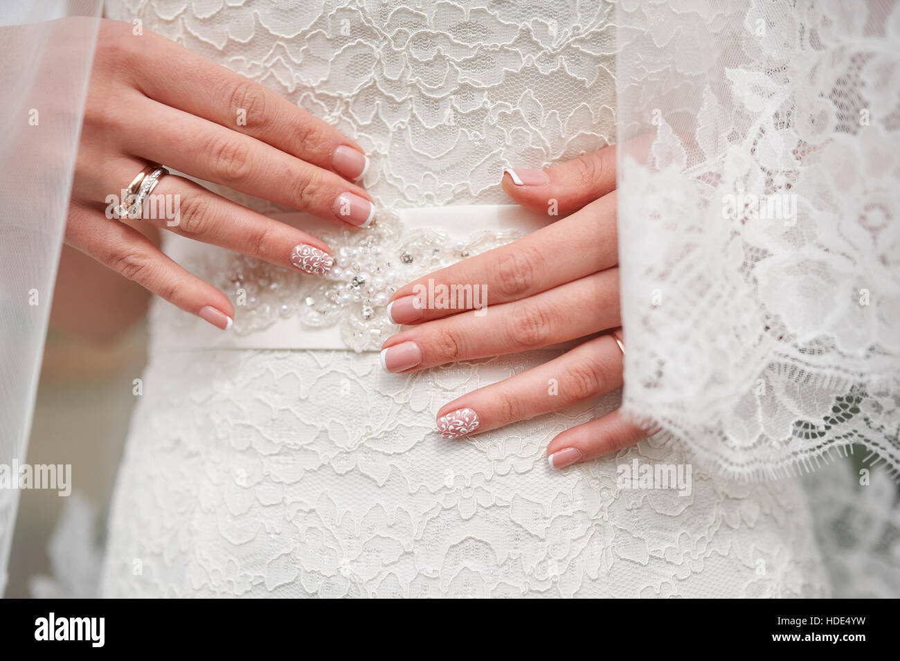 Les mains de la mariée avec une manucure sur robe blanche, close-up Banque D'Images