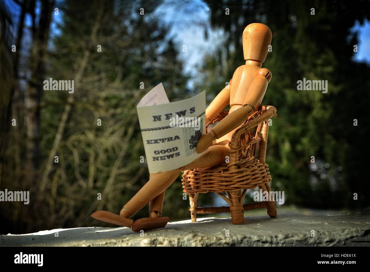 Figure en bois assis sur chaise de patio et reading newspaper Banque D'Images