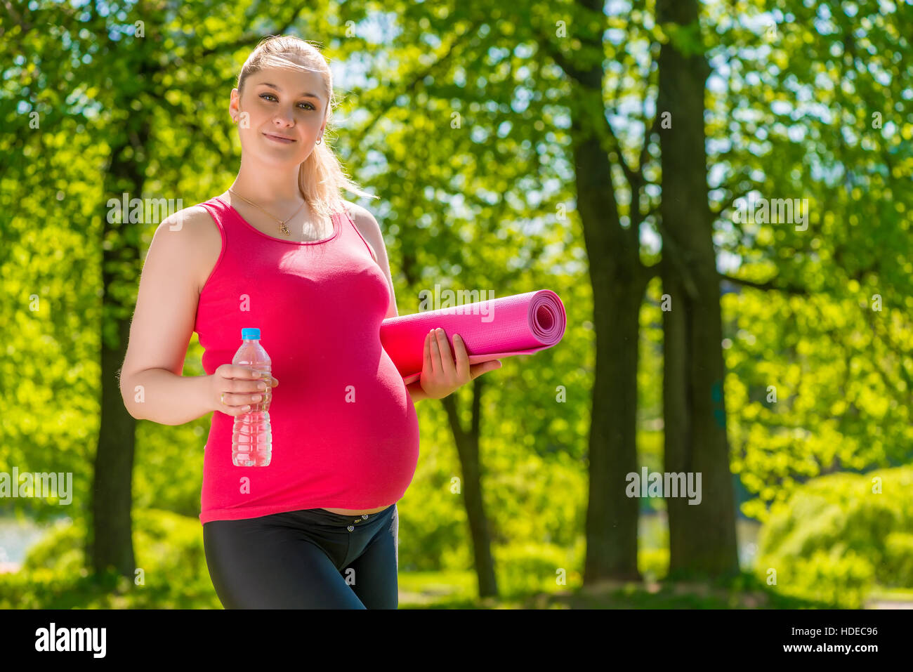 Femme enceinte d'apparence de race blanche d'un tapis et de l'eau après l'exercice dans la nature Banque D'Images