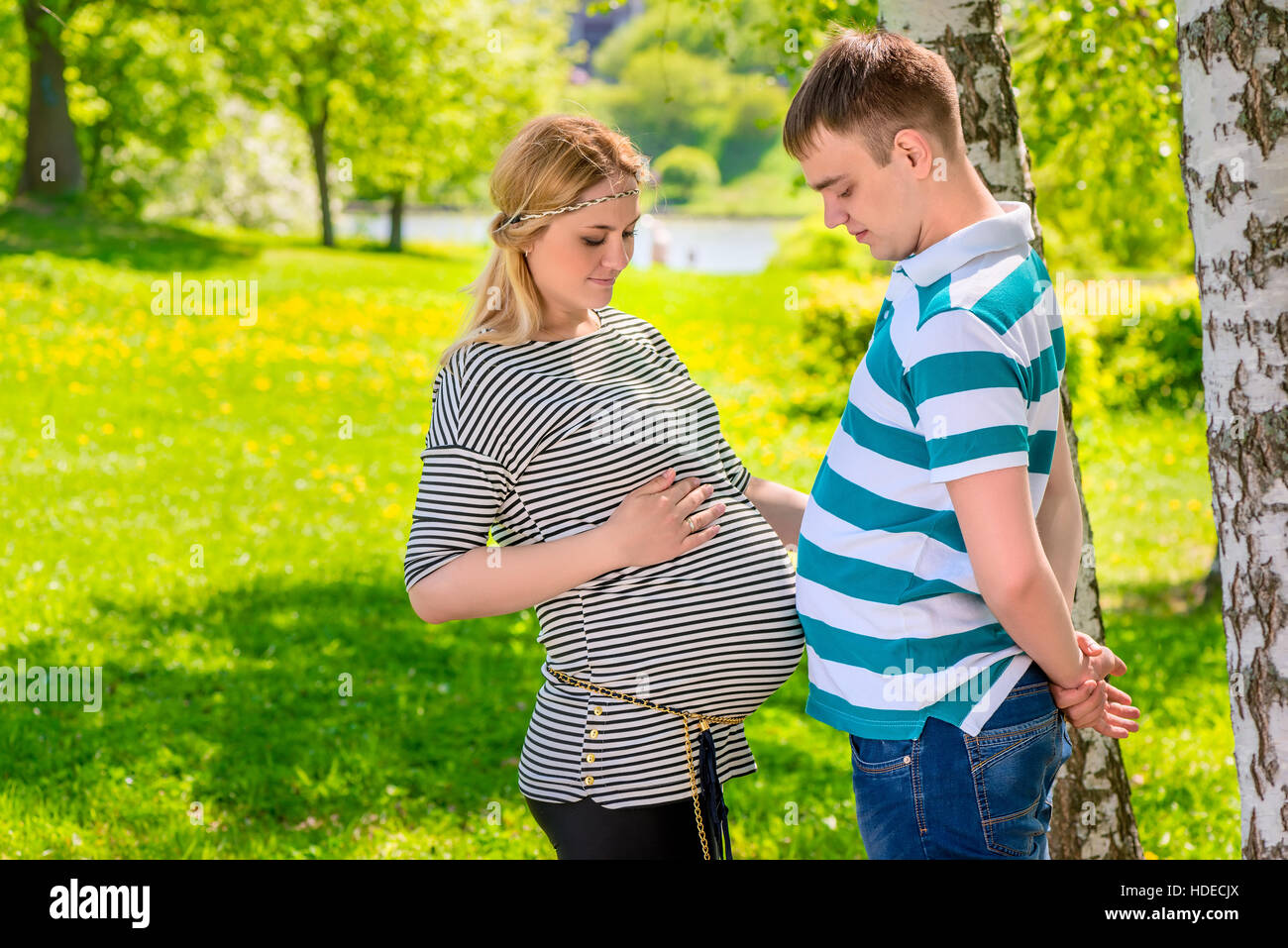 Homme et femme enceinte comparer leurs estomacs, tourné dans le parc jour d'été Banque D'Images