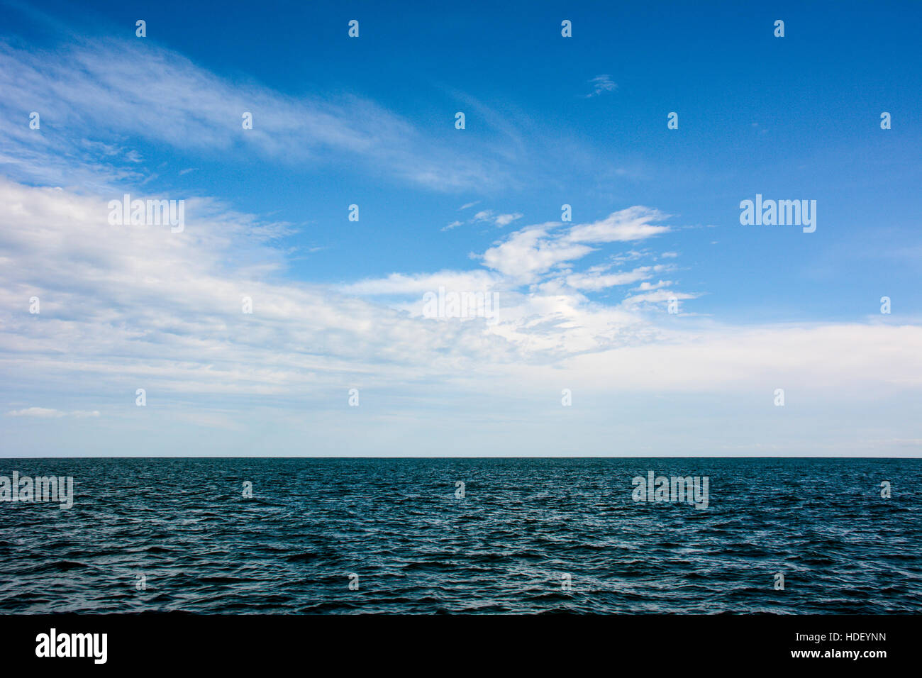 Blanc à motifs de nuages dans un ciel bleu sur une mer d'azur ondulé. Banque D'Images