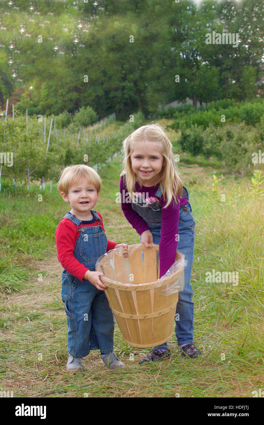 Frère et soeur adorables frères holding basket portant des bretelles debout dans ferme pour la cueillette des pommes à l'automne automne Banque D'Images