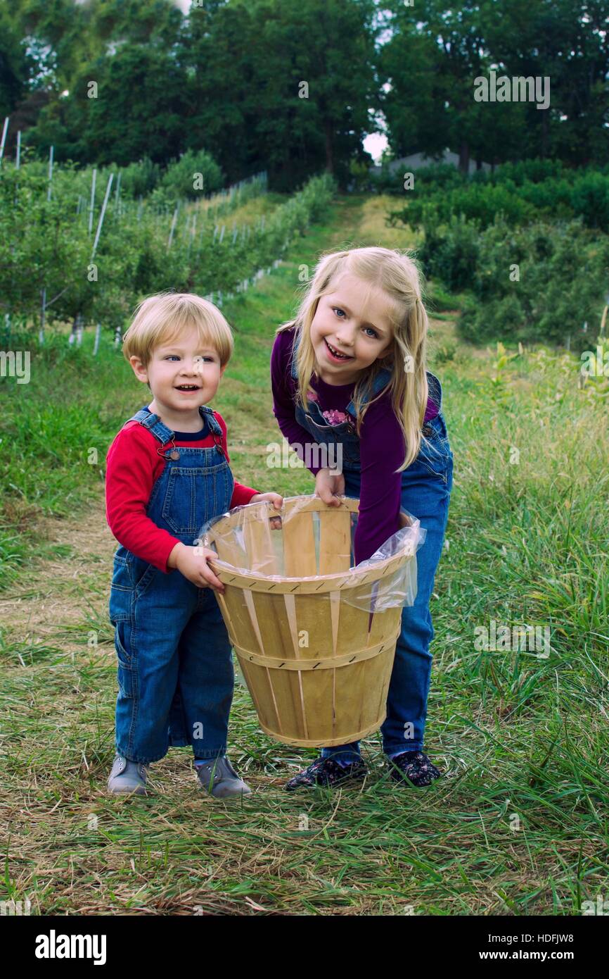 Frère et soeur adorables frères holding basket portant des bretelles debout dans ferme pour la cueillette des pommes à l'automne automne Banque D'Images