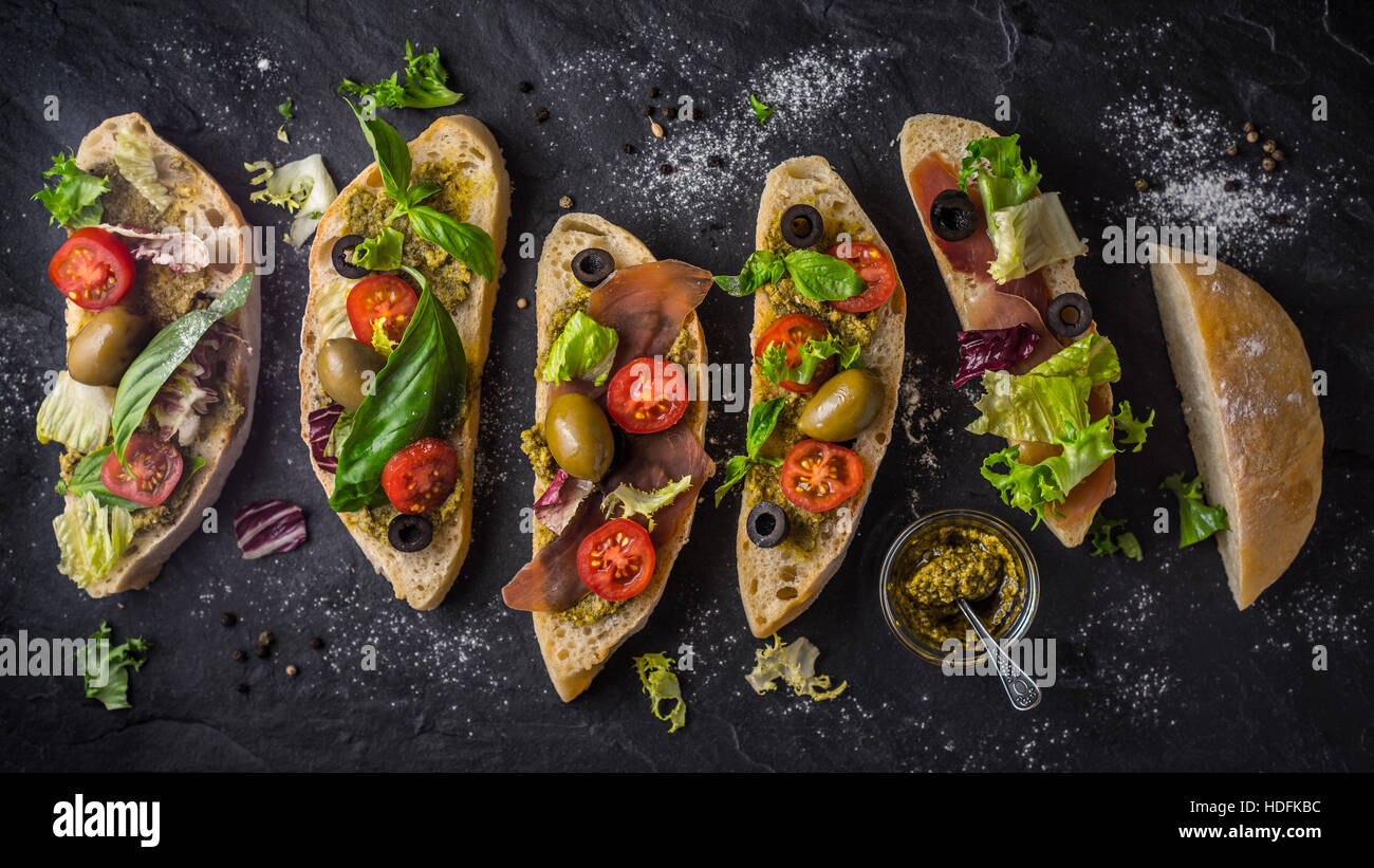 Tranches de pain ciabatta aux olives, tomates et basilic sur le grand écran noir table de pierre Banque D'Images