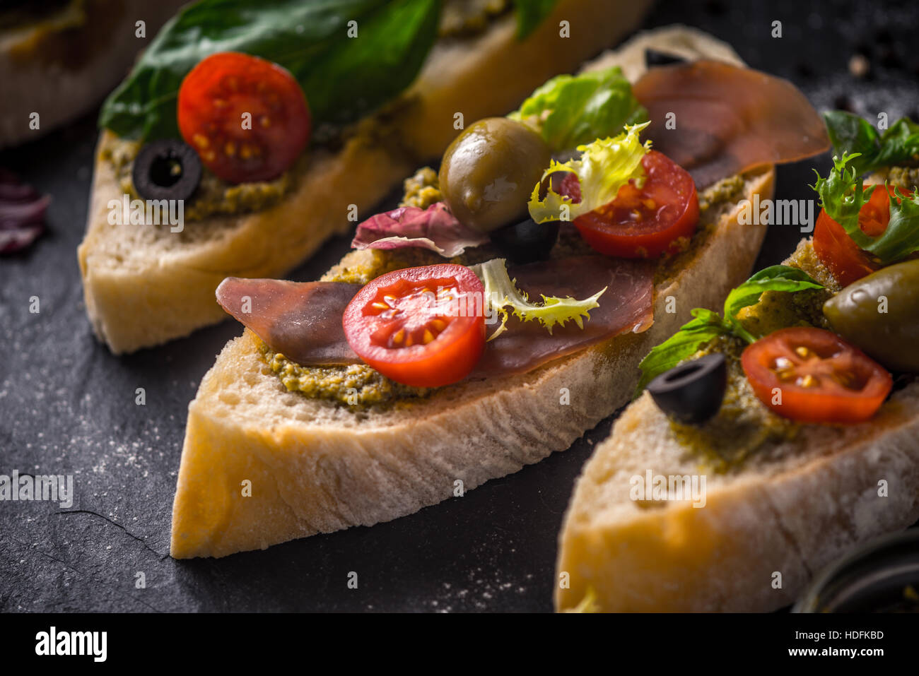 Tranches de pain ciabatta aux olives, tomates et basilic sur la pierre noire table horizontale Banque D'Images