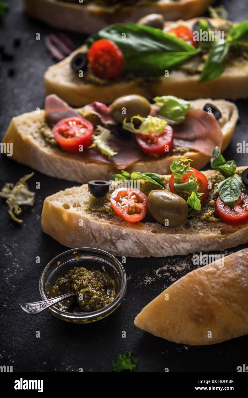 Tranches de pain ciabatta aux olives, tomates et basilic sur la pierre noire table verticale Banque D'Images