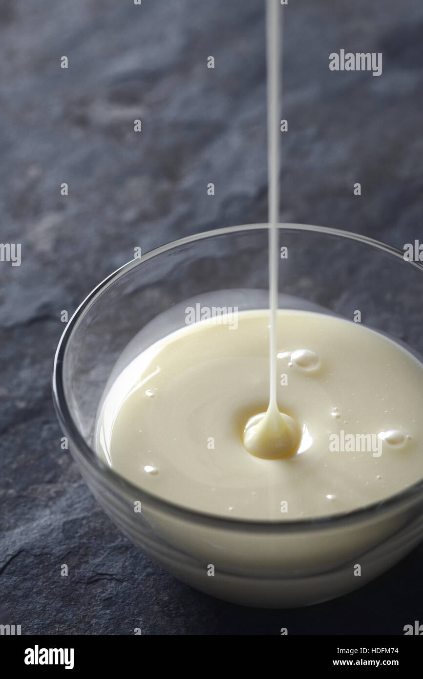 Verser le lait condensé dans le bol en verre à la verticale Banque D'Images