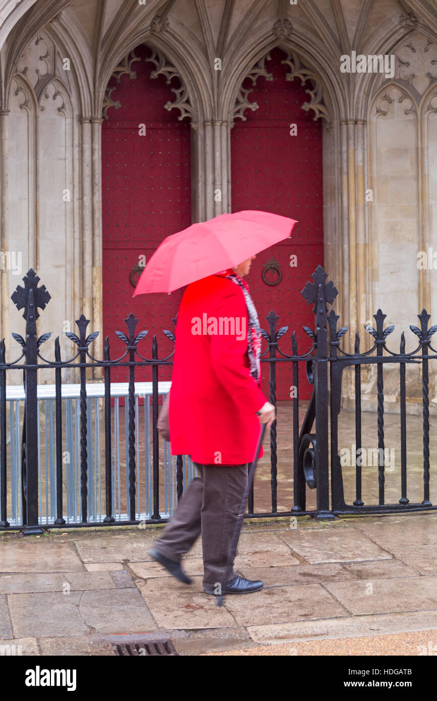 Winchester, Hampshire, Royaume-Uni 12 décembre 2016. Lady se dépêche le long passé de la rue la cathédrale de Winchester en essayant de garder sec sous parapluie rouge sur un jour de bruine humide à la Winchester en décembre. Credit : Carolyn Jenkins/Alamy Live News Banque D'Images
