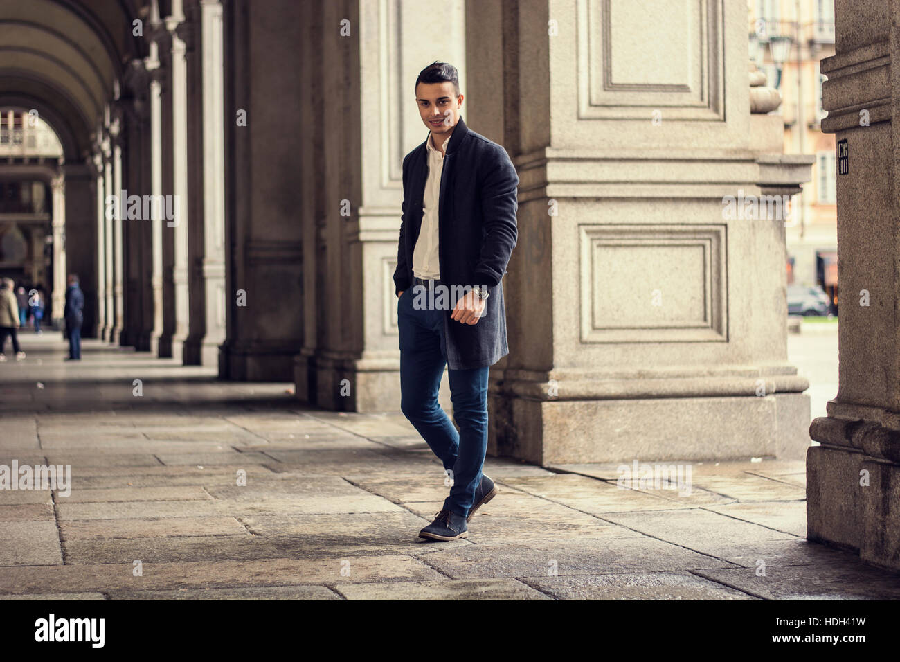 Jeune homme tenant à la main dans la poche de marcher à travers la galerie à Turin en Italie et à la recherche à l'appareil photo. Banque D'Images