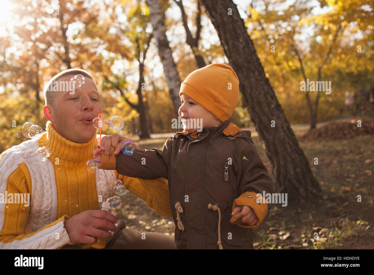 Père faisant des bulles avec bébé garçon dans le parc en automne Banque D'Images