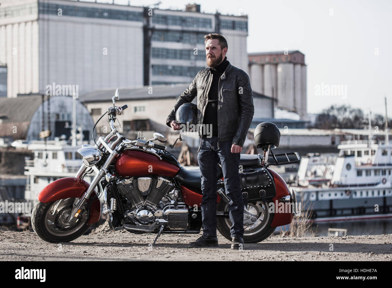 Portrait du motard tenue casque tout en se tenant en moto contre l'environnement industriel Banque D'Images