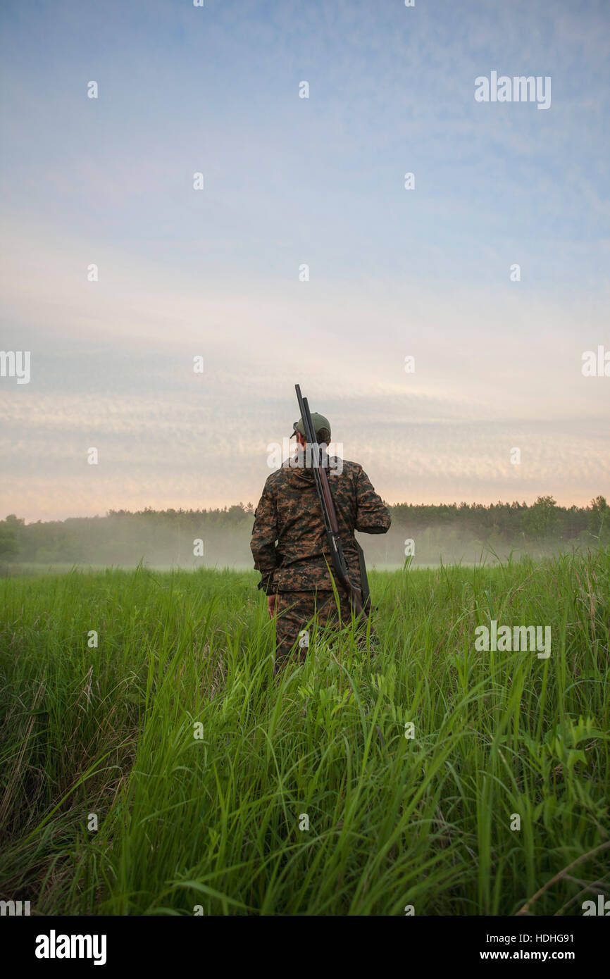 Vue arrière du hunter debout à Grassy field against sky Banque D'Images
