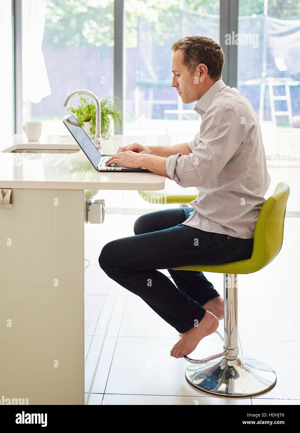 Un homme assis sur une chaise de cuisine au comptoir, à l'aide d'un ordinateur portable. Banque D'Images