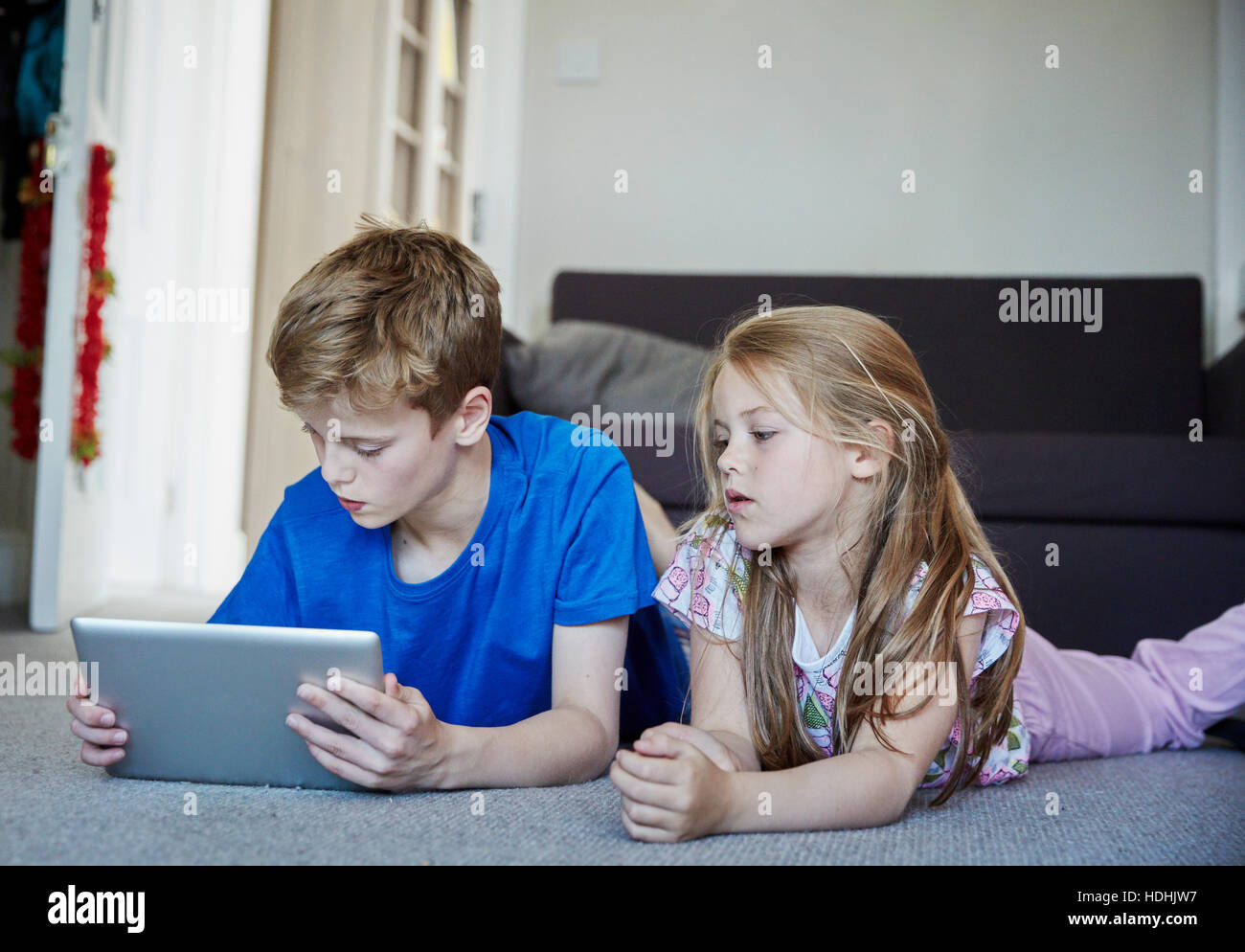 Deux enfants allongés sur le ventre le partage d'une tablette numérique à regarder l'écran. Banque D'Images
