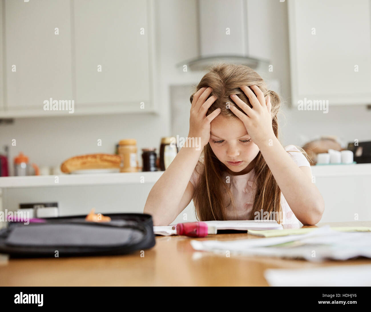 Une fille assise à une table avec ses mains sur sa tête, regardant ses devoirs. Banque D'Images