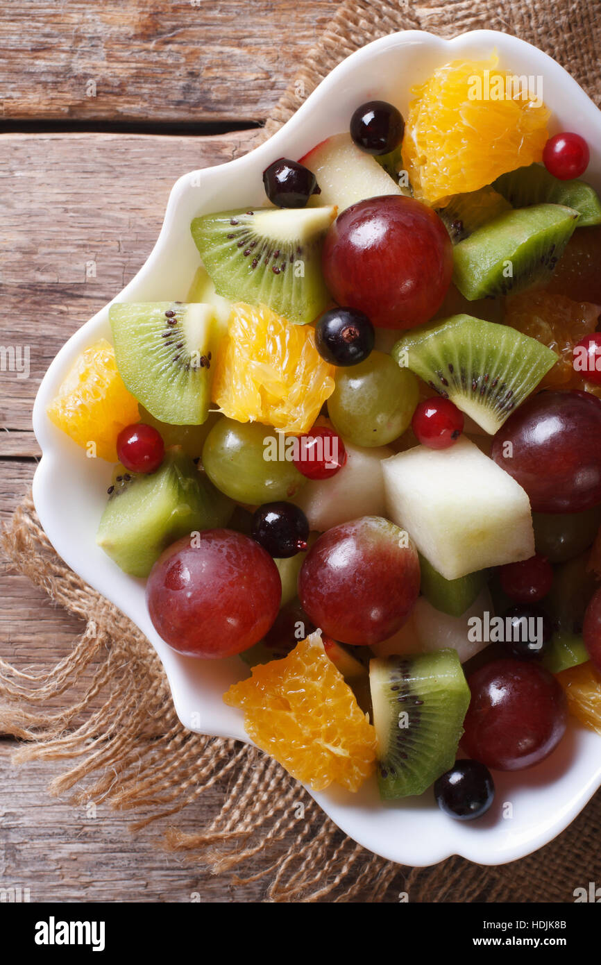 Salade de fruits en plaque blanche sur la table de près. Vue verticale de ci-dessus, style rustique Banque D'Images