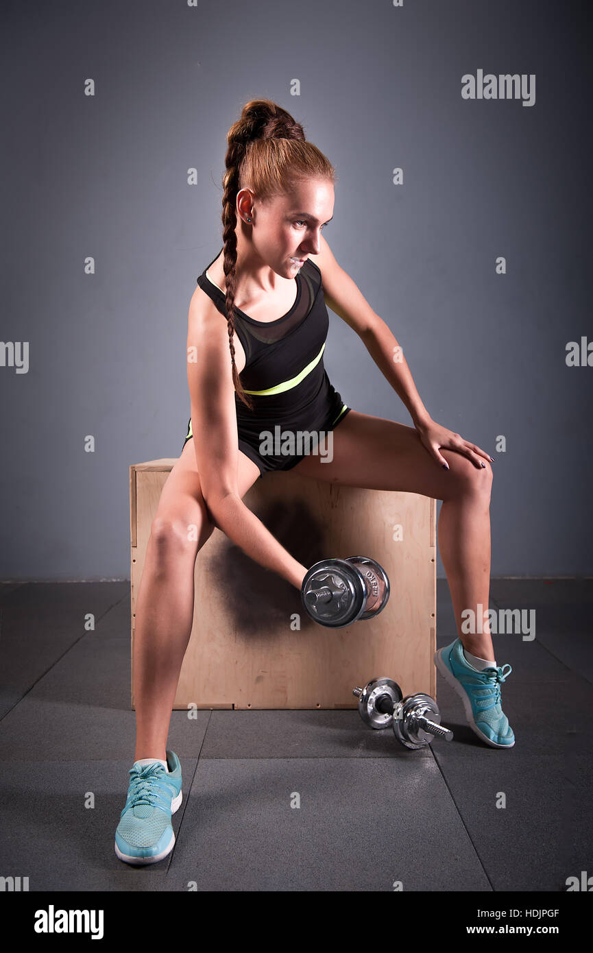 Jeune femme confiante biceps faisant de l'exercice avec haltères en centre de remise en forme. Formation fille mince dans la salle de sport Banque D'Images