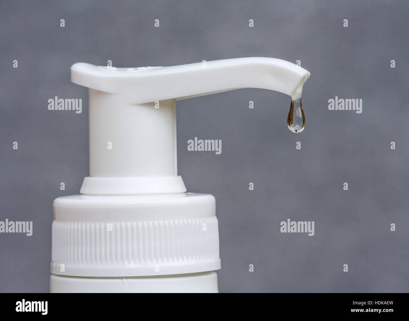 Libre d'une goutte transparente suspendue à un distributeur de savon sur un fond gris. Banque D'Images