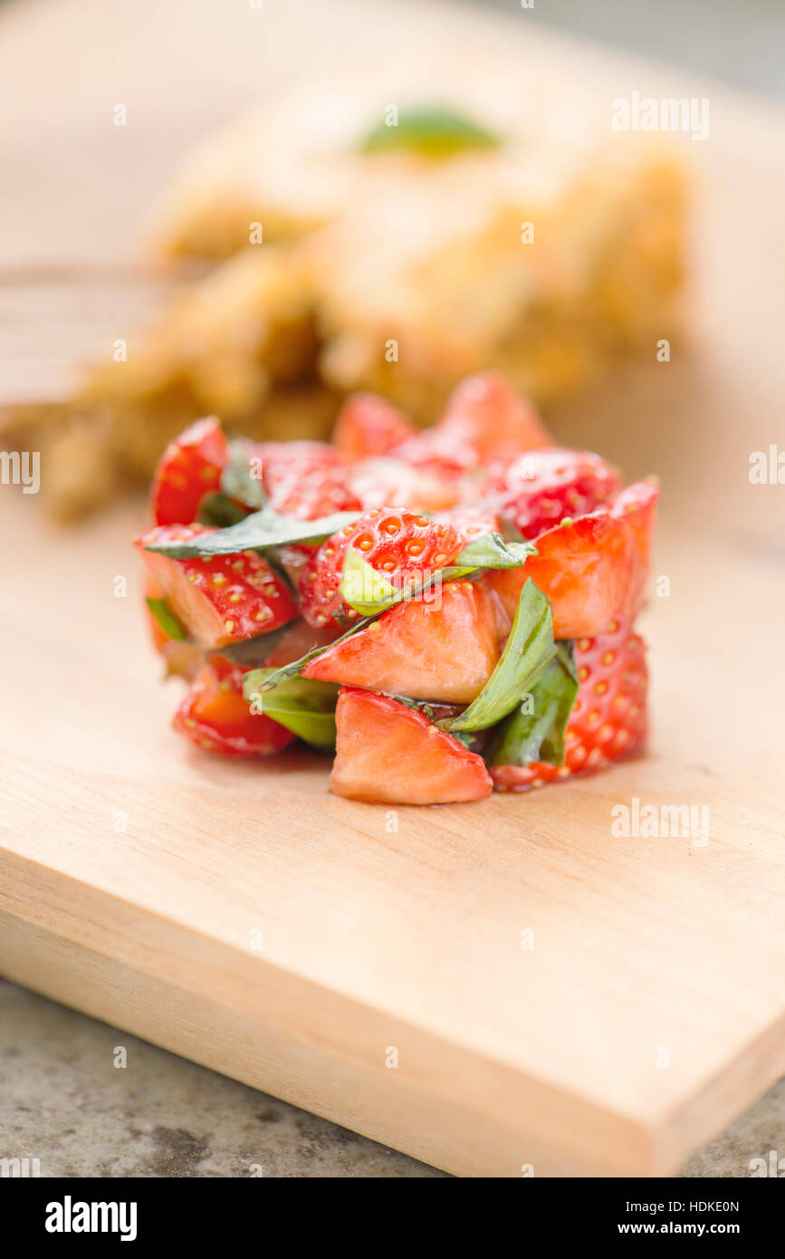 Des fraises et de feuilles de basilic frais marinés au vinaigre balsamique. Gâteau de carotte dans l'arrière-plan. Banque D'Images
