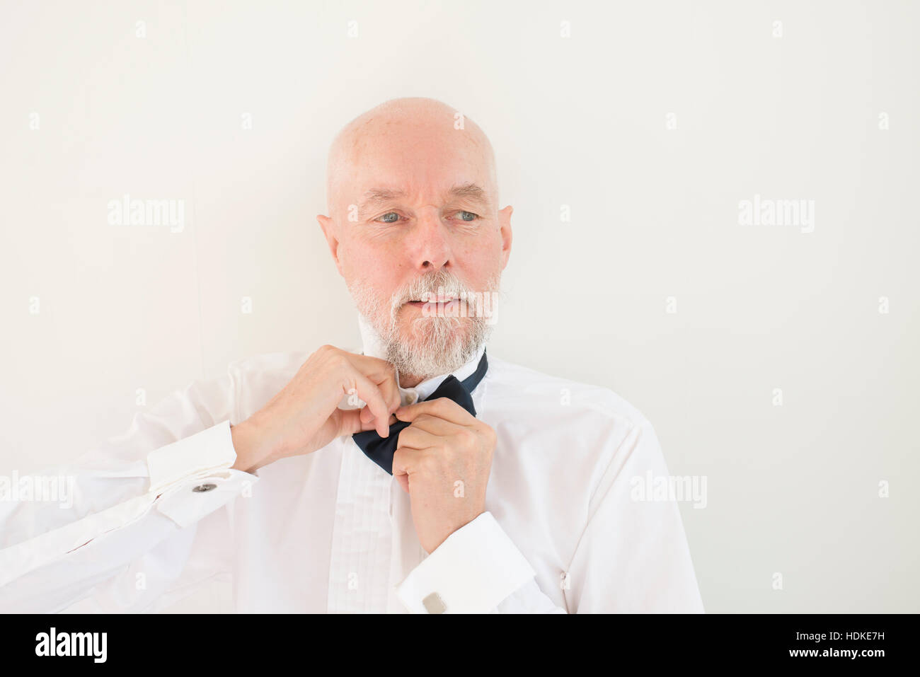 Old man putting on black bowtie et chemise blanche à la maison. Moment de vie de retraite active et la préparation de mariage ou élégante occasion. Banque D'Images