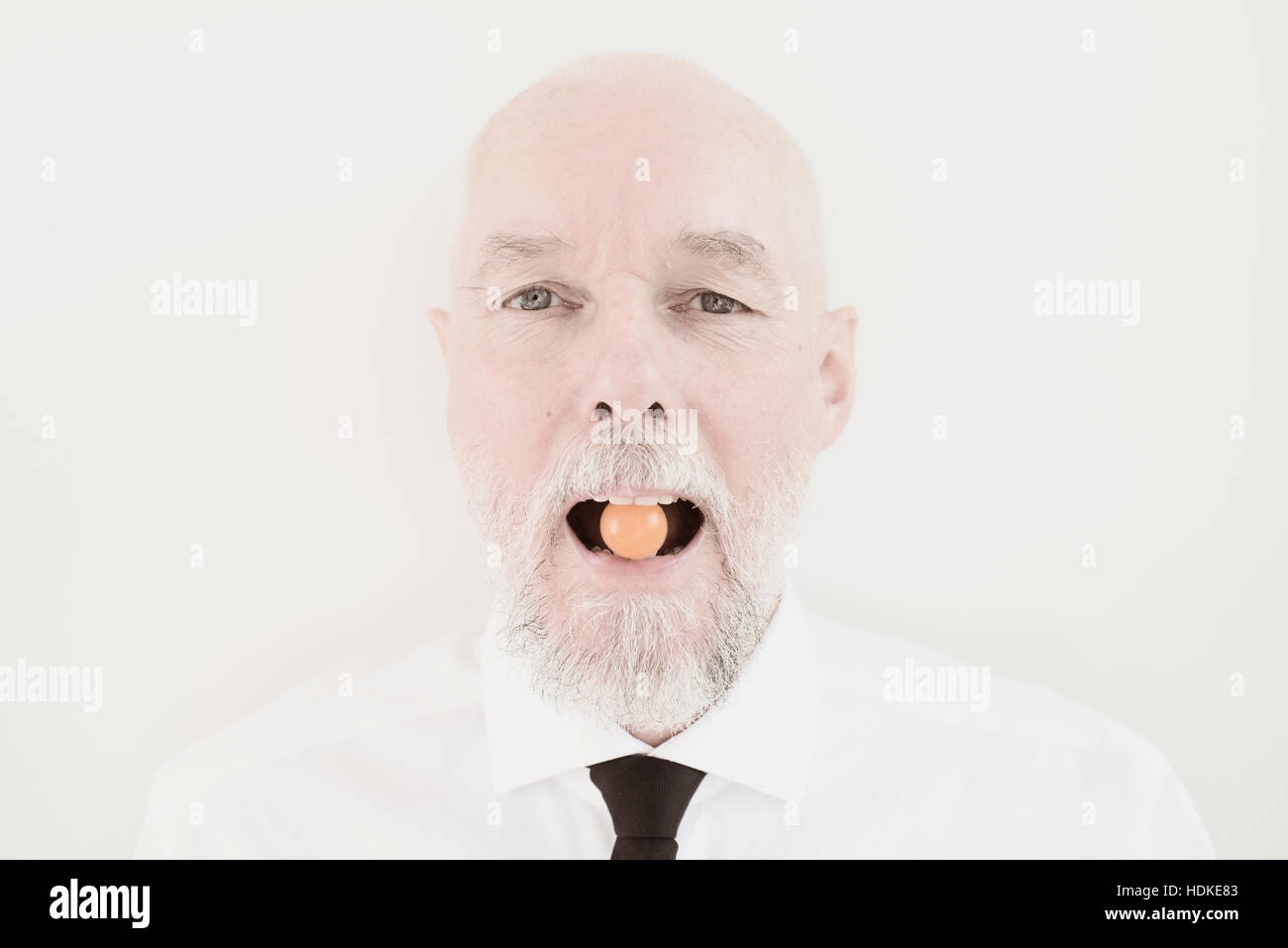 Portrait de vieil homme avec petite tomate dans sa bouche. Drôle et instant ludique. Image conceptuelle d'un mode de vie sain et manger des légumes en tant que senior Banque D'Images
