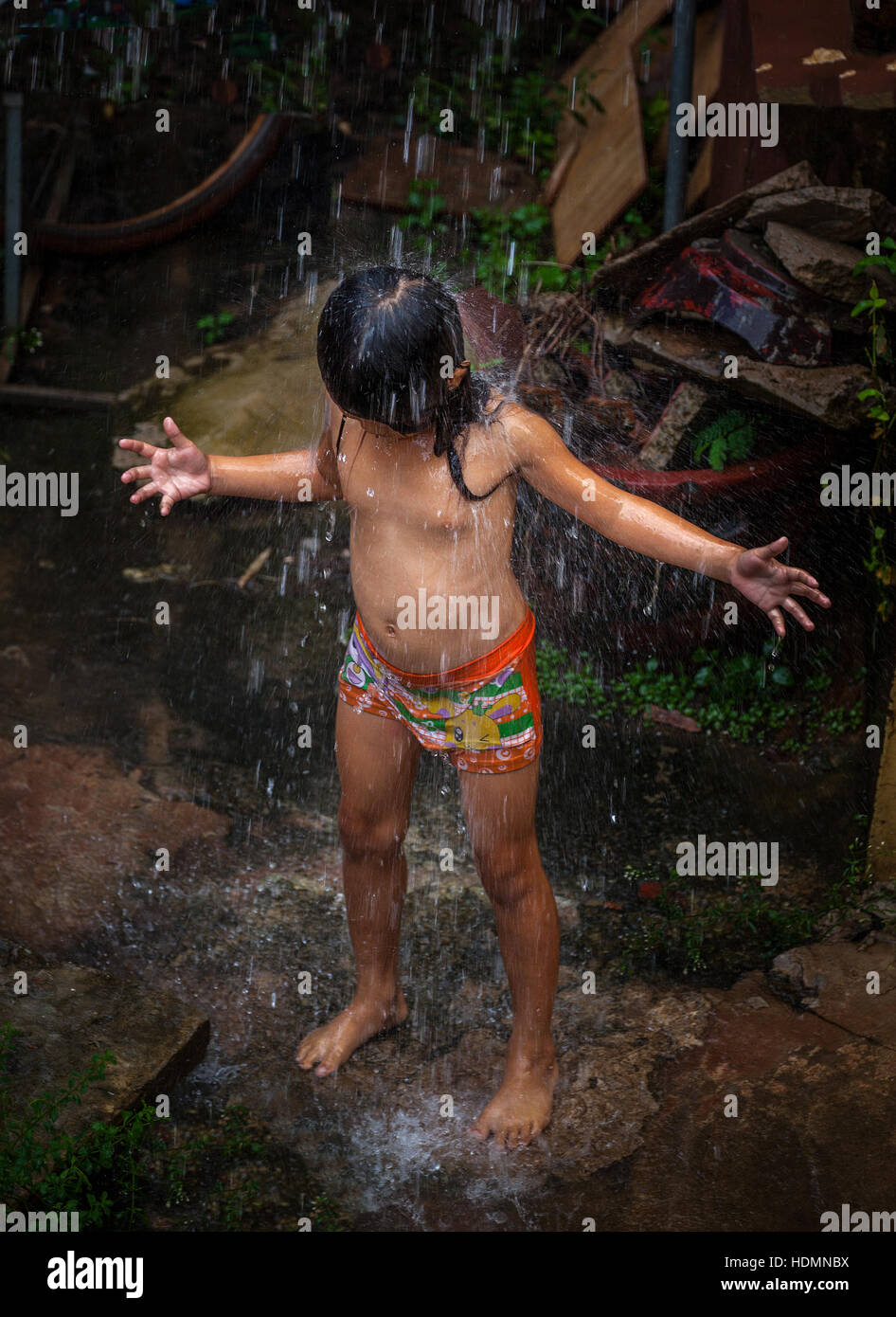 Un jeune enfant Khmer cambodgien cools elle-même en versant l'eau de pluie à partir d'une descente à Siem Reap, Royaume du Cambodge. Banque D'Images