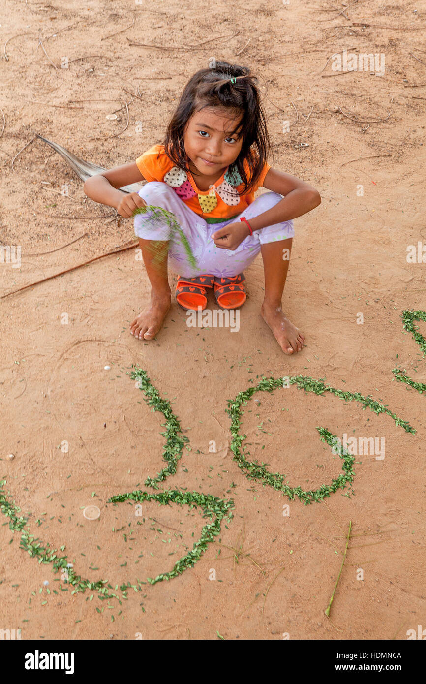 Un enfant de cinq ans fille cambodgienne apprend son alphabet Khmer à l'aide de morceaux de feuilles disposées dans la terre au Cambodge. Banque D'Images