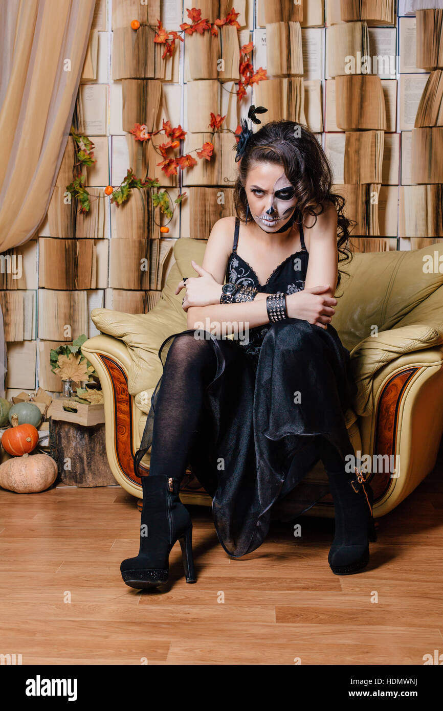 Jeune femme en noir avec la moitié du crâne face make-up ion assis au fauteuil. Banque D'Images