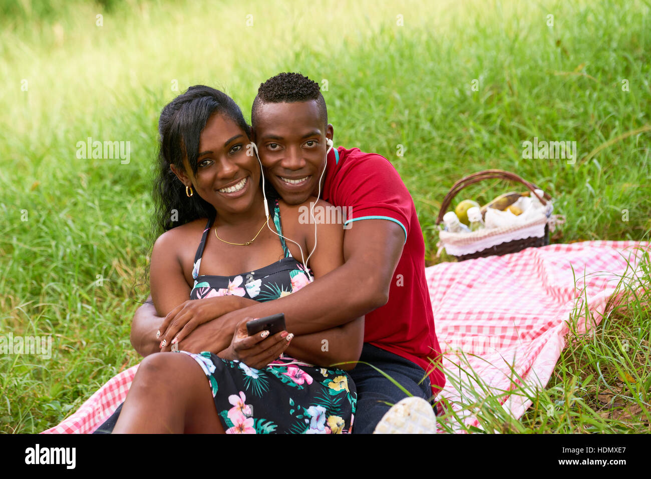 Happy black couple having fun in city park. Young african american man and woman listening to music on mobile phone and smiling. Banque D'Images