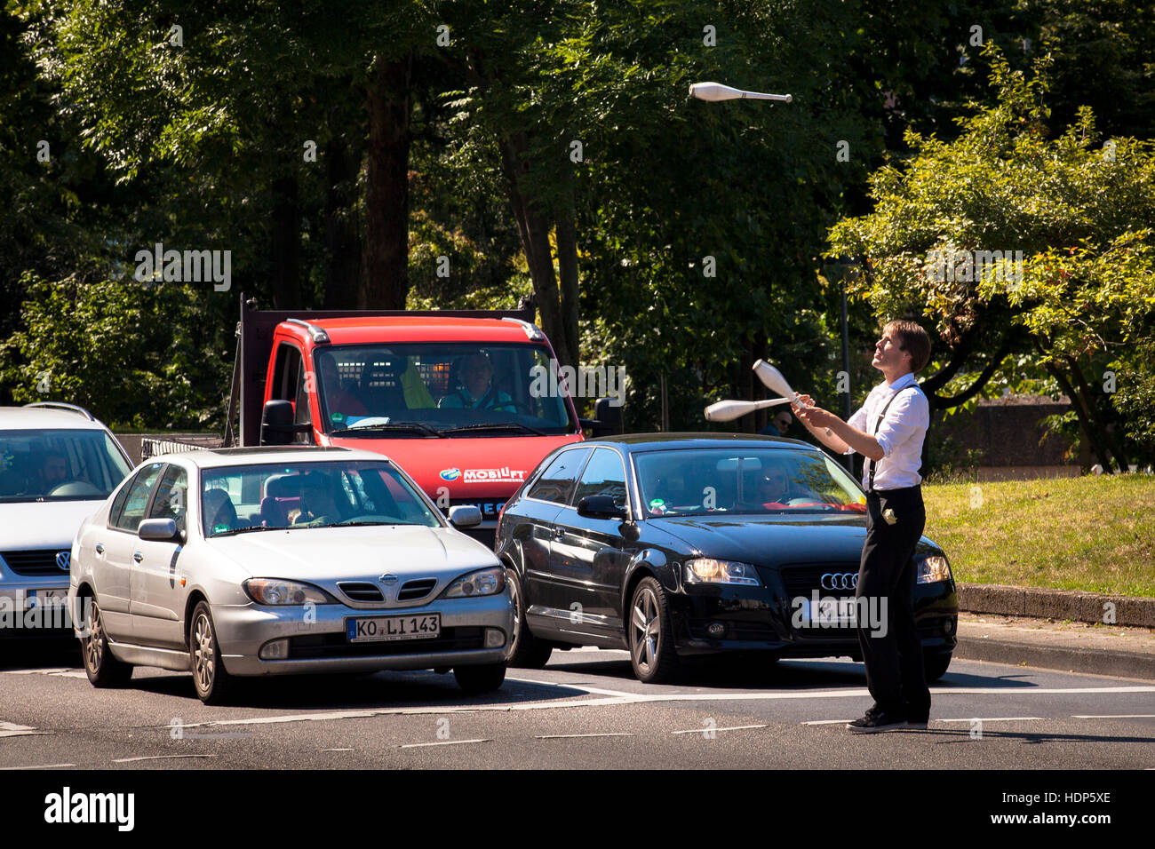 Allemagne, Cologne, jongleur, à l'avant des voitures, l'attente aux feux de circulation, après l'exercice il demande les pilotes pour un don. Banque D'Images