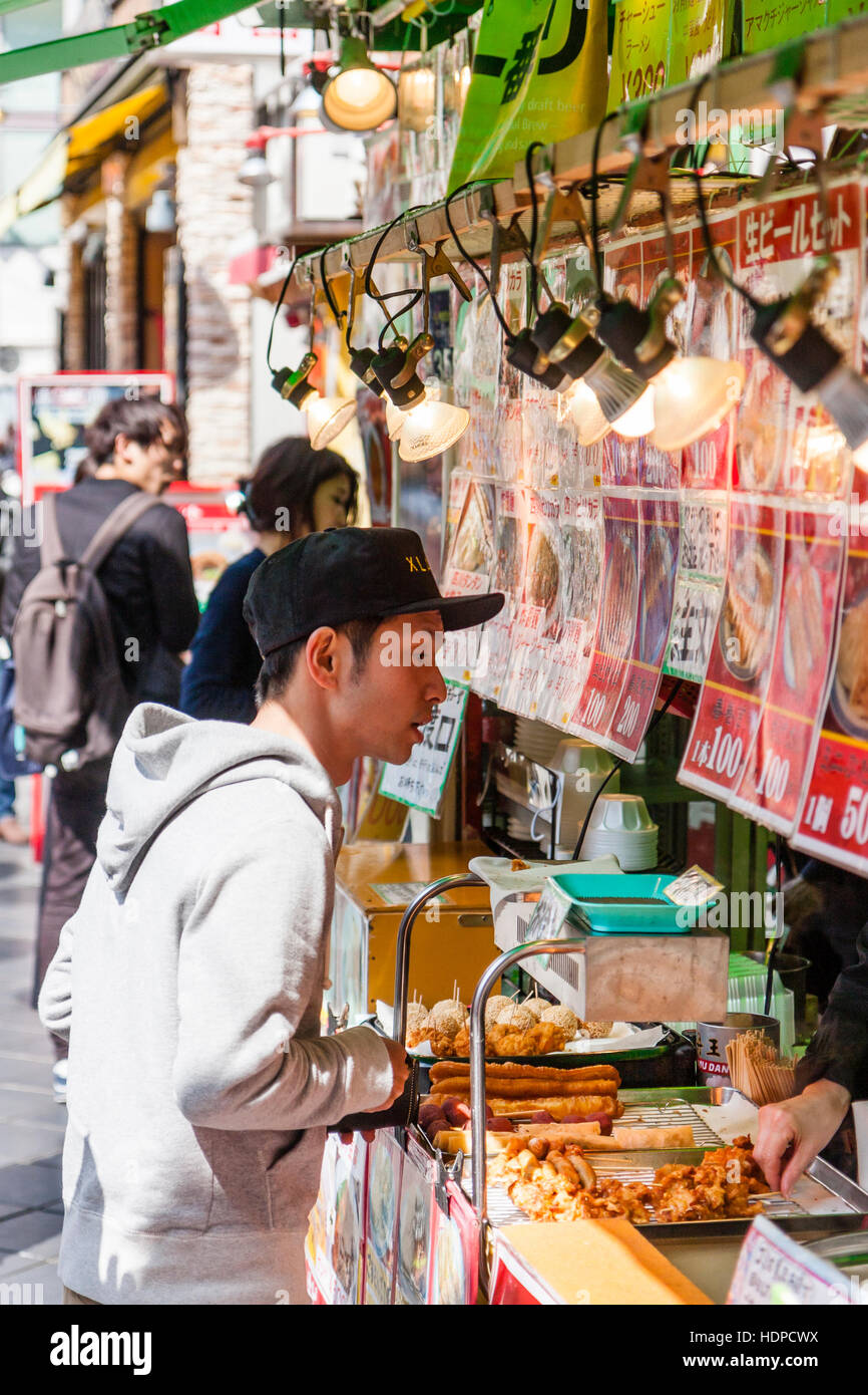 Le Japon, Kobe Nankinmachi, Chinatown. Jeune homme japonais avec chapeau de base-ball, de l'alimentation commande de compteur à emporter chinois de la nourriture chaude, wc séparés. Banque D'Images