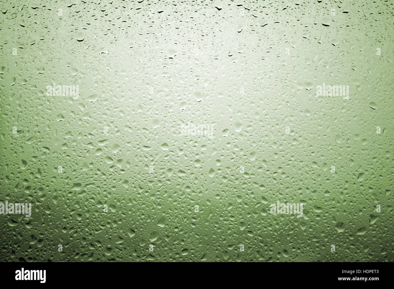 Gouttes de pluie sur une vitre de fenêtre avec paysage très diffuse de couleur vert jaunâtre Banque D'Images