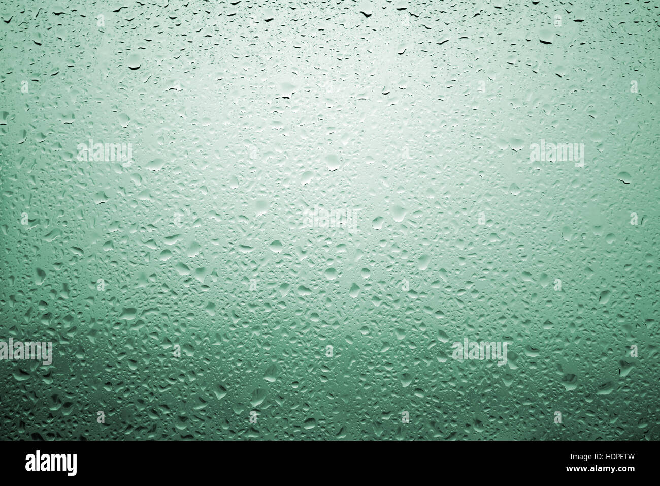 Gouttes de pluie sur une vitre de fenêtre avec paysage très diffuse de couleur vert bleuâtre Banque D'Images